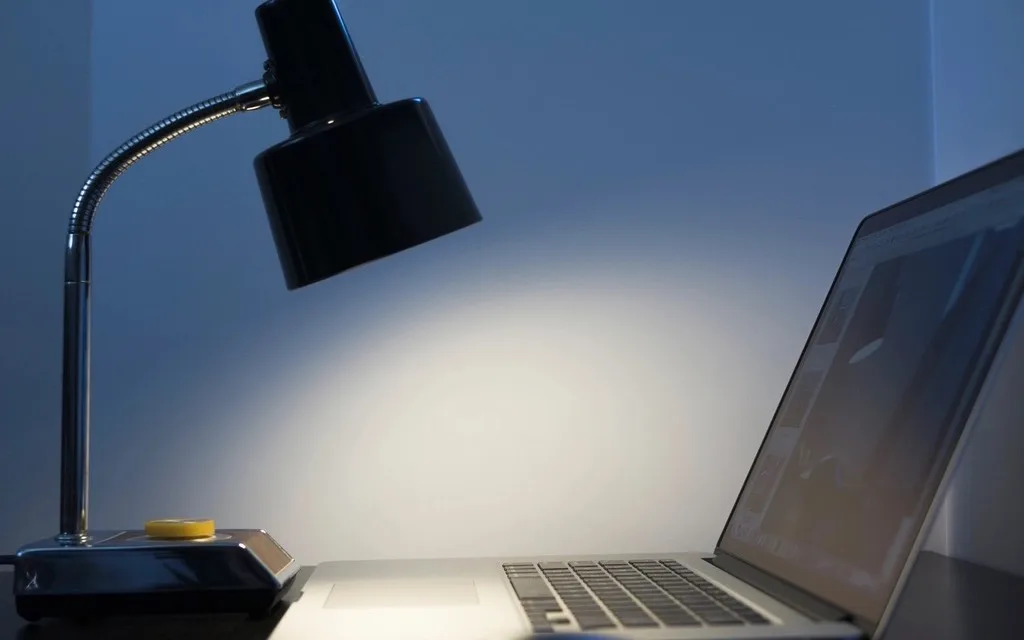 Eine Schwanenhals-Schreibtischlampe beleuchtet einen dunklen Schreibtisch neben einem aufgeklappten Laptop