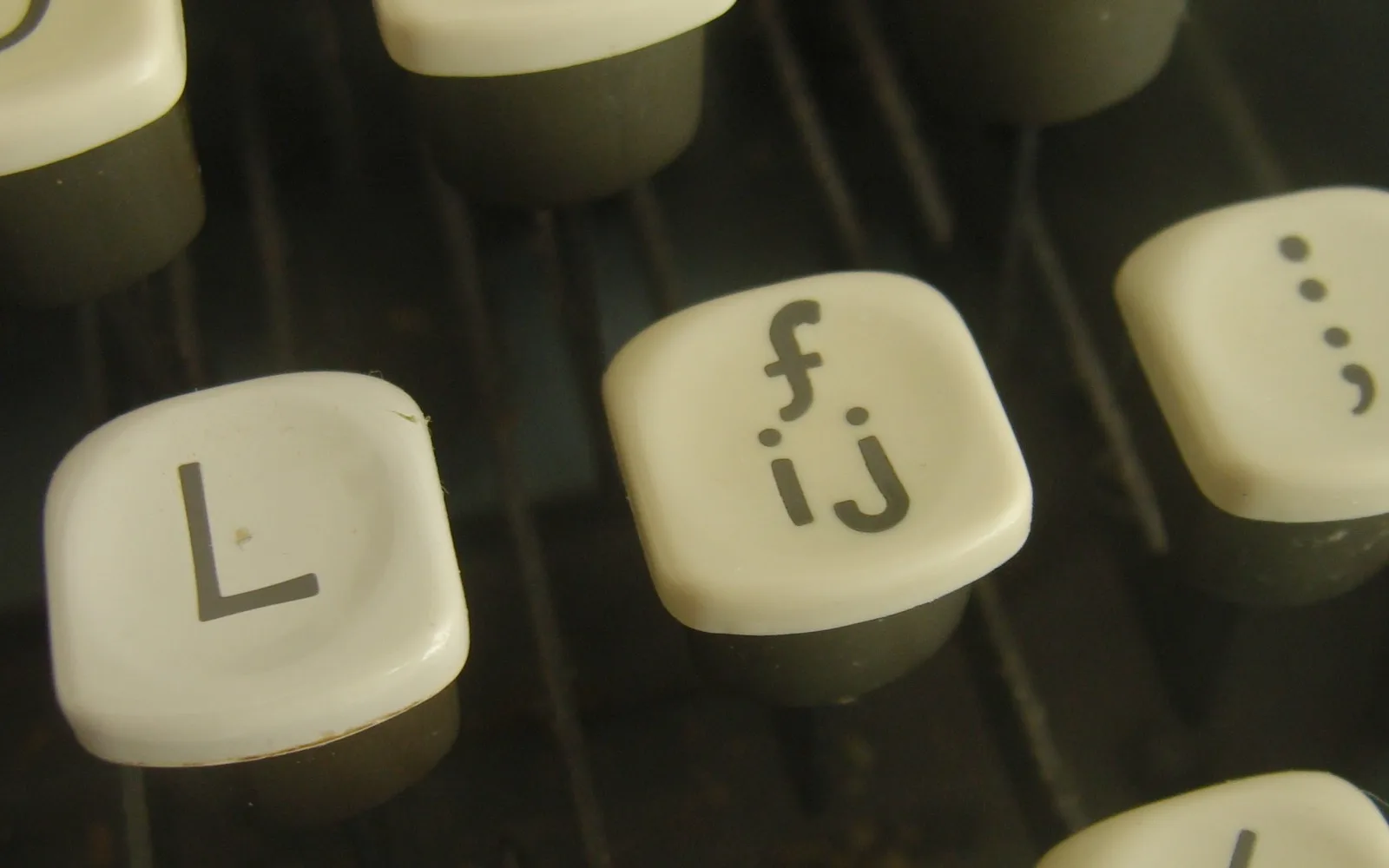 Primo piano di tasti di una macchina da scrivere color crema, tra cui un tasto L e un tasto con f e ij