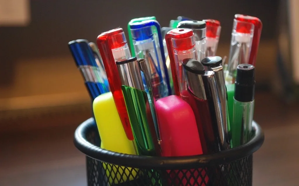 Un portapenne in rete nera con penne e evidenziatori colorati su una scrivania