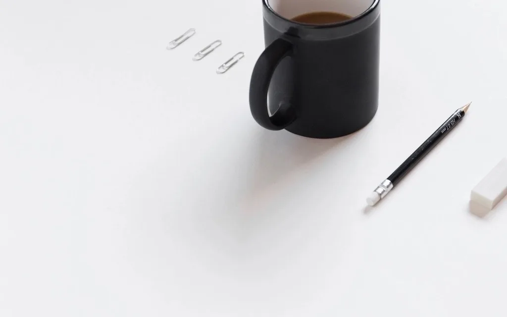 A pencil, an eraser, paper clips and a black coffee mug on a white desk
